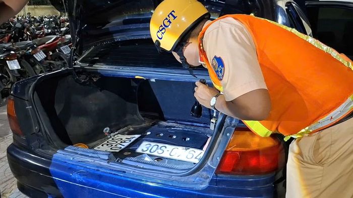 Cảnh sát giao thông kiểm tra ở cốp sau của xe ô tô có 2 biển số màu trắng.