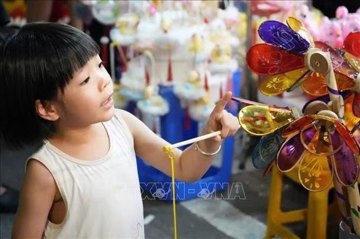 Một em nhỏ thích thú lựa chọn đồ chơi nhiều màu sắc tại cửa hàng trên phố Hàng Mã.