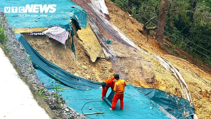 Đoạn taluy bị sụt lún, đất đá trôi trượt xuống bên dưới tạo thành hàm ếch rộng. Các công nhân dùng bạt che chắn để hạn chế nước mưa làm đất đá tiếp tục chảy trượt.