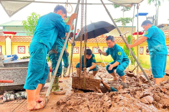 Làm việc trong bùn nhão, lấy ô che mưa để đưa hài cốt liệt sĩ về khu vực lấy mẫu sinh phẩm an toàn. Ảnh: Tùng Phương