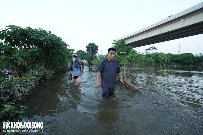Ông T. (áo xanh nhạt) cho biết quen với cảnh cầu tạm Tân Phú ngập nước mỗi khi có mưa lớn. Hiện cầu bị ngập từ ngày 17/9 đến nay nước vẫn chưa rút. Do làm việc tại khu vực này nên ông phải mang cất quần áo dài để lội qua sông, sau đó thay đồ ở bờ bên kia để đến nơi làm việc.