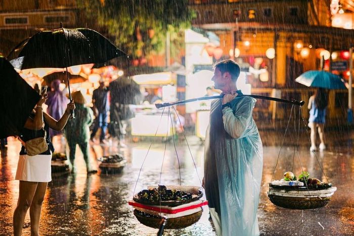 Du khách nước ngoài vui vẻ trải nghiệm gánh hàng rong dưới cơn mưa tầm tã của Hội An