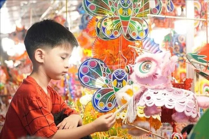 Một em nhỏ thích thú lựa chọn đồ chơi Trung thu truyền thống tại cửa hàng trên phố Hàng Mã trong những ngày cận Rằm tháng Tám. Ảnh: Quốc Lũy/TTXVN