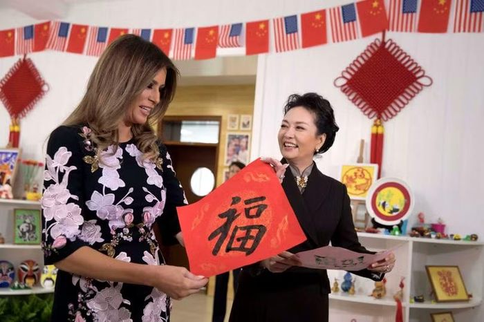 Đệ nhất phu nhân Mỹ Melania Trump và đệ nhất phu nhân Trung Quốc Bành Lệ Viện cùng giơ cao bức thư pháp chữ Hán có nghĩa "vận may" do các em học sinh viết trong chuyến thăm trường tiểu học Banchang ở Bắc Kinh vào tháng 11/2017. Ảnh: Reuters.