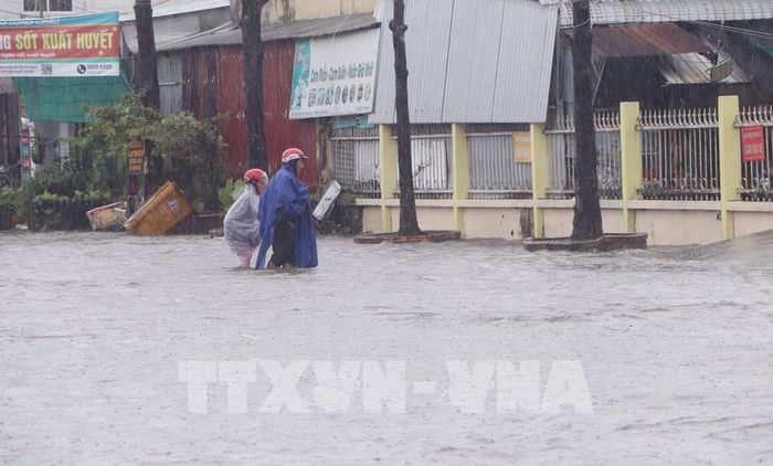 Người dân hỗ trợ người già di chuyển qua những điểm ngập sâu tại tuyến đường trung tâm tỉnh Cà Mau. Ảnh: Tuấn Phi - TTXVN 