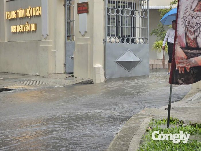 Nước chảy cuồn cuộn ra mặt đường, tạo thành các vòng xoáy sâu, cản trở người tham gia giao thông.