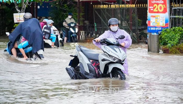 Xe điện, xe gắn máy chật vật qua đoạn nước sâu, trong khi sóng nước do ô tô chạy qua khiến việc di chuyển thêm khó khăn.