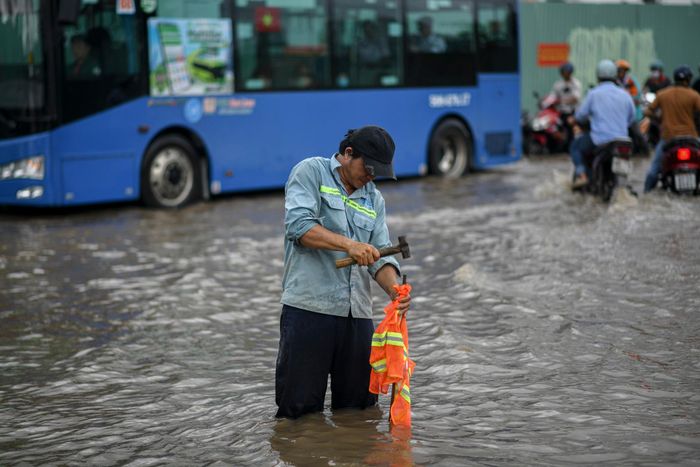 Một công nhân của công trường gần đó dùng búa đóng cọc sắt gắn áo phản quang để đánh dấu vị trí nguy hiểm, ổ gà.