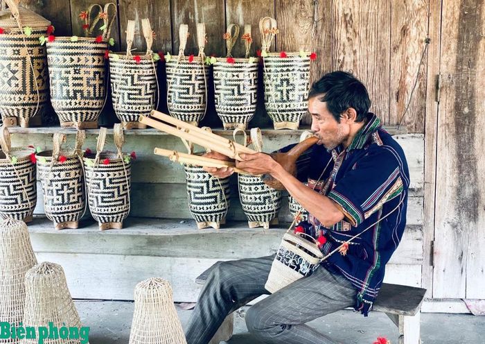 Nghệ nhân Ntơr Ha Bang thổi kèn bầu trong lúc nghỉ tay đan lát. Ảnh: H.N.T