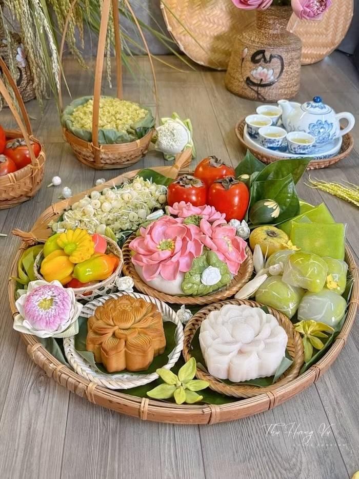 “Mâm Cỗ Mùa Trăng” của chị Thu Hương Vũ gây ấn tượng bởi cách kết hợp những thức quà đặc trưng của mùa thu như cốm non, lúa mới, hồng chín, sen và trà cùng những chiếc bánh Trung thu tạo hình thủ công. Trên chiếc mẹt tre mộc mạc, các nguyên liệu được sắp đặt hài hòa, gợi không khí Rằm tháng Tám đậm nét truyền thống