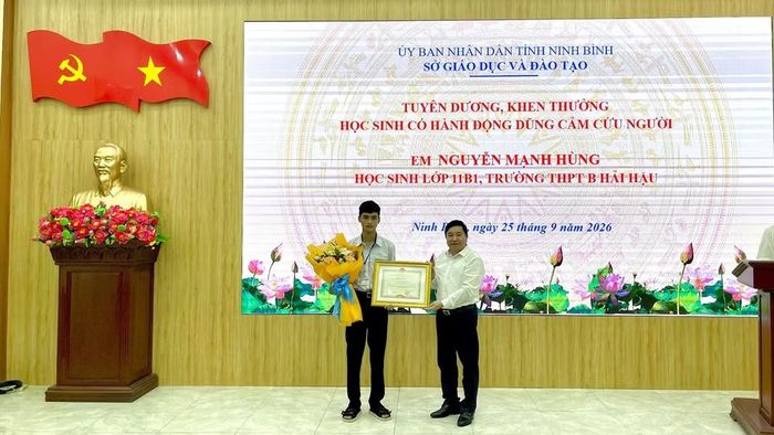 Đồng chí Nguyễn Tiến Dũng, Giám đốc Sở Giáo dục và Đào tạo tỉnh Ninh Bình trao Bằng khen của Chủ tịch Ủy ban nhân dân tỉnh và tặng hoa cho em Nguyễn Mạnh Hùng. (Ảnh: YẾN TRINH)