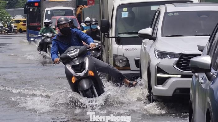 Người đàn ông đi xe máy bất ngờ sụp ổ gà, loạng choạng tay lái suýt ngã khi đang cố gắng phi nhanh qua đoạn đường ngập nước. Ảnh: Khoa Nam.