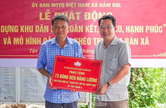 Ông Lê Tấn Công, Phó Chủ tịch UBND xã Đầm Dơi (bên phải), trao bảng tượng trưng tặng bóng đèn năng lượng mặt trời cho khu dân cư, góp phần hoàn thiện hạ tầng nông thôn.