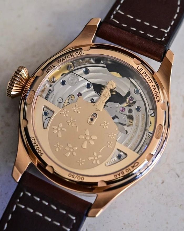 Từ năm 2013, hãng Thuỵ Sĩ IWC bắt đầu đưa Le Petit Prince (Hoàng tử bé) của nhà văn kiêm phi công Pháp Antoine de Saint-Exupéry vào dòng Pilot’s Watch. Theo Hodinkee, những phiên bản này dễ nhận biết nhờ mặt số xanh midnight blue cùng hình ảnh nhân vật Hoàng tử bé ở mặt sau. Một trong những thiết kế thể hiện mối liên hệ với nguyên tác rõ nhất là Big Pilot’s Watch Perpetual Calendar Edition “Le Petit Prince”, với đĩa tuần trăng ở góc 12 giờ tái hiện Hoàng tử bé đứng trên tiểu hành tinh nhìn lên bầu trời, dựa trên chính minh họa của Saint-Exupéry. Rotor của bộ máy cũng mang huy chương vàng hình nhân vật này. Ảnh: Monochrome Watches.