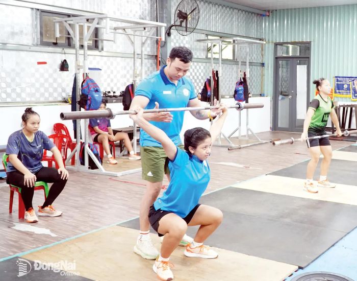 Huấn luyện viên hướng dẫn vận động viên cử tạ chống đỡ ngồi sâu, hỗ trợ động tác giật.