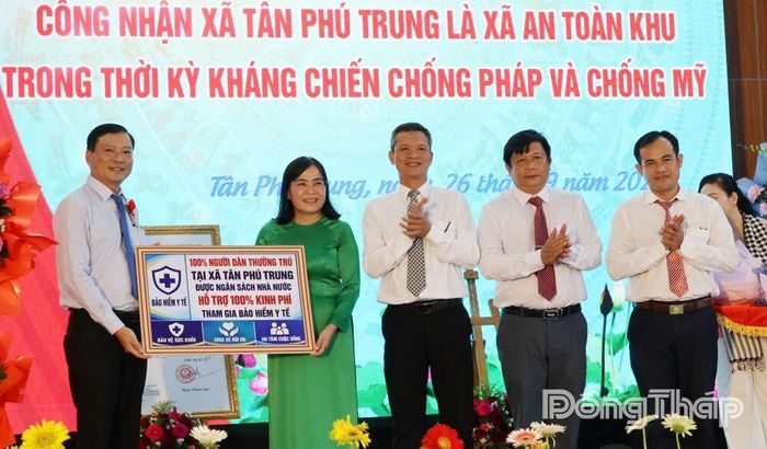 Đại diện địa phương nhận bảng tượng trưng hỗ trợ 100% kinh phí tham gia bảo hiểm y tế cho người dân thường trú trên địa bàn xã Tân Phú Trung. Ảnh: KIM PHỤNG