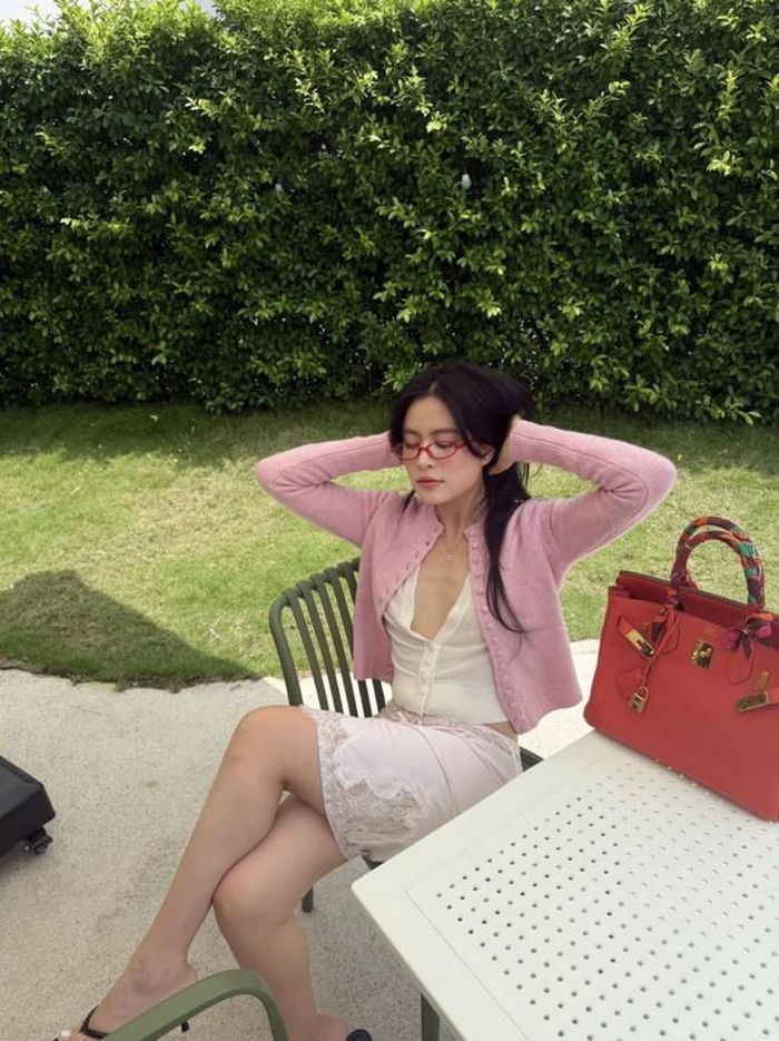Cô diện chiếc cardigan màu hồng pastel kết hợp chân váy ren trắng, mái tóc buông xõa tự nhiên cùng điểm nhấn là chiếc kính gọng đỏ siêu nhỏ đúng chuẩn xu hướng thịnh hành của các fashionista.