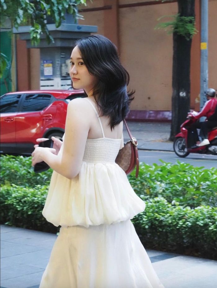 Trong một outfit, cô diện set đồ mang tông trắng kem gồm áo hai dây dáng bí phối ren kết hợp cùng chân váy dài. Sự kết hợp này mang đến tổng thể nữ tính, thướt tha và bay bổng, rất hợp để diện đi chơi, dạo phố hay tận hưởng những ngày cuối tuần.