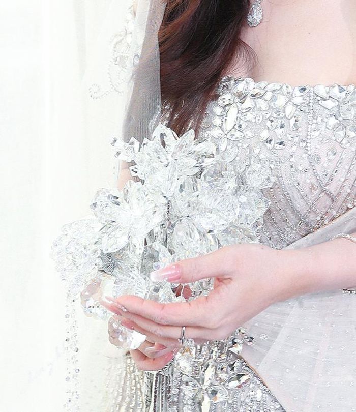 Hoàn thiện bộ áo cưới là bó hoa cưới bằng pha lê được tạo hình độc đáo thay vì hoa tươi như thường lệ. Những khối pha lê trong suốt, lấp lánh dưới ánh đèn tượng trưng cho tình yêu tinh khiết, rực rỡ và hạnh phúc của đôi uyên ương trong ngày trọng đại.