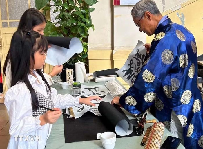 Nghệ sỹ Vũ Cẩn hướng dẫn các em nhỏ làm quen với nghệ thuật thư pháp trong chương trình Tết Trung Thu tại Arcueil, ngoại ô phía Nam Paris. (Ảnh: Trần Đức Hùng/TTXVN)
