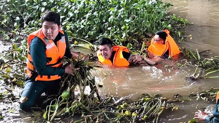 Cán bộ, chiến sĩ và người dân cùng dầm mình dưới nước vớt lục bình và rác để khơi thông dòng chảy. Ảnh: Bảo Long