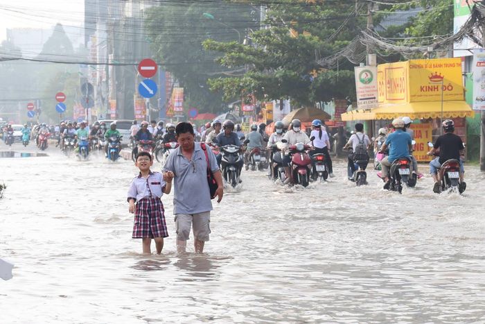  Anh Thái Hoàng (ngụ Cần Thơ) cho biết mực nước đến nửa bánh xe máy tại một số tuyến đường thuộc phường Bình Thủy gây khó trong việc đưa con đến trường. Anh phải di chuyển chậm để tránh văng nước vào quần áo của con. Ảnh chụp tại đường Cách Mạng Tháng 8 sáng 28/9. Ảnh: Trung Phạm. 