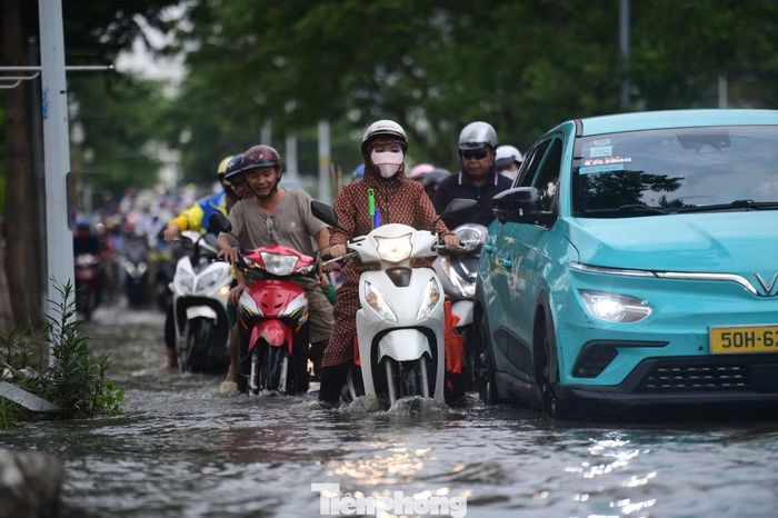 Nhiều người đi xe máy phải chạy lên vỉa hè để tránh đoạn đường ngập. Các phương tiện di chuyển qua khu vực này chậm hơn bình thường, một số xe phải giảm tốc độ để tránh nước tràn vào động cơ.