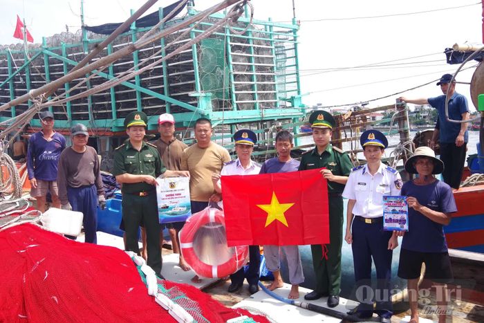 Cảnh sát biển và Bộ đội Biên phòng trao tặng cờ Tổ quốc, quà và tuyên truyền chống khai thác IUU cho ngư dân tại Cảng cá Nhật Lệ - Ảnh: Q.N