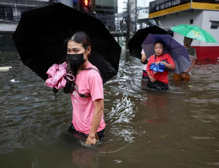  Người dân mang vác đồ tạp hóa di chuyển qua khu vực bị ngập lụt. (Ảnh: Reuters)