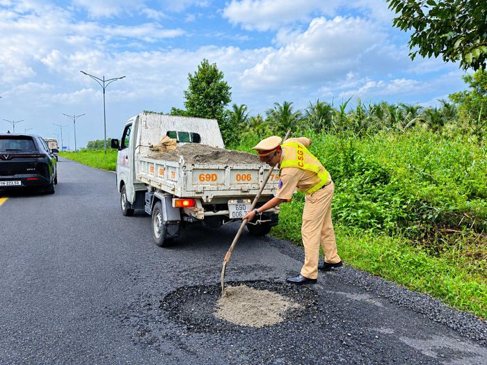 Lực lượng CSGT vận động vật tư, dặm vá ổ gà điểm lên xuống cầu. Ảnh: Ký Long