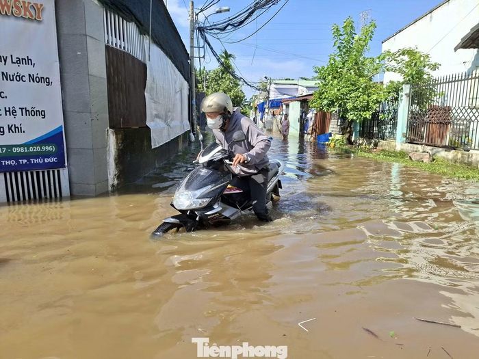 Người dân chật vật di chuyển qua khu vực ngập sâu tại hẻm 84 đường số 11, phường Thủ Đức.