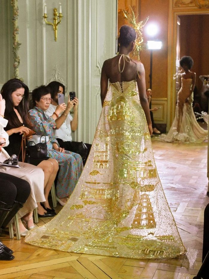 “Merci Paris,” một trong những thiết kế dụng công nhất của bộ sưu tập. Cấu trúc áo yếm truyền thống được phát triển thành đầm dạ hội cổ yếm phủ kim sa vàng. Trên tà váy, bốn công trình Eiffel, Versailles, cầu Trường Tiền và chùa Linh Mụ được tạo hình bằng pha lê và kim sa, mất khoảng hai tháng để hoàn thiện thủ công. (Ảnh: NVCC)