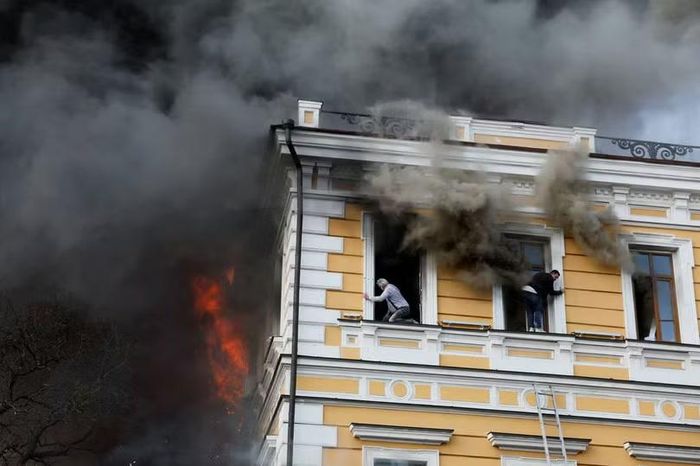 Hai người đàn ông thoát ra ngoài qua cửa sổ khi khói bốc lên nghi ngút từ một tòa nhà ở Kiev bị trúng bom bởi máy bay không người lái. Ảnh: Reuters.