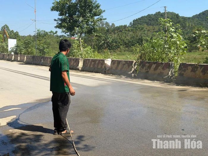Người dân trên tuyến Đường tỉnh 526B tưới nước để chống bụi bay vào nhà.