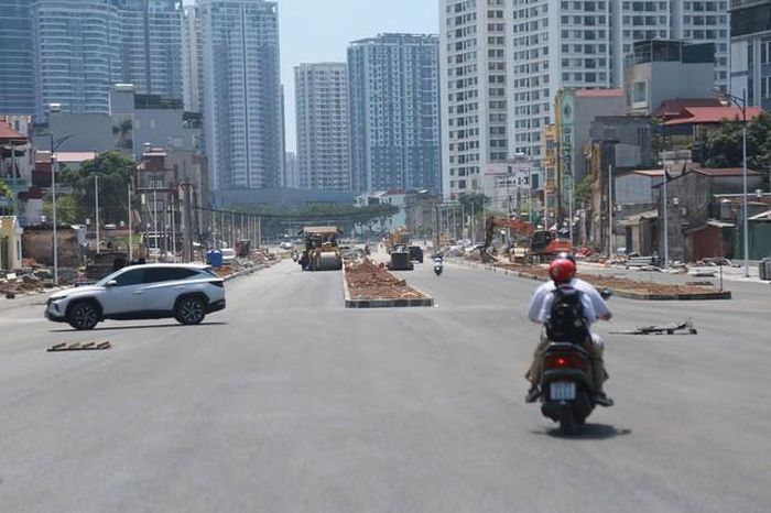 Người dân di chuyển trên mặt đường mới thảm nhựa trong khi các máy móc cơ giới phía xa vẫn tiếp tục hoàn thiện hạ tầng.