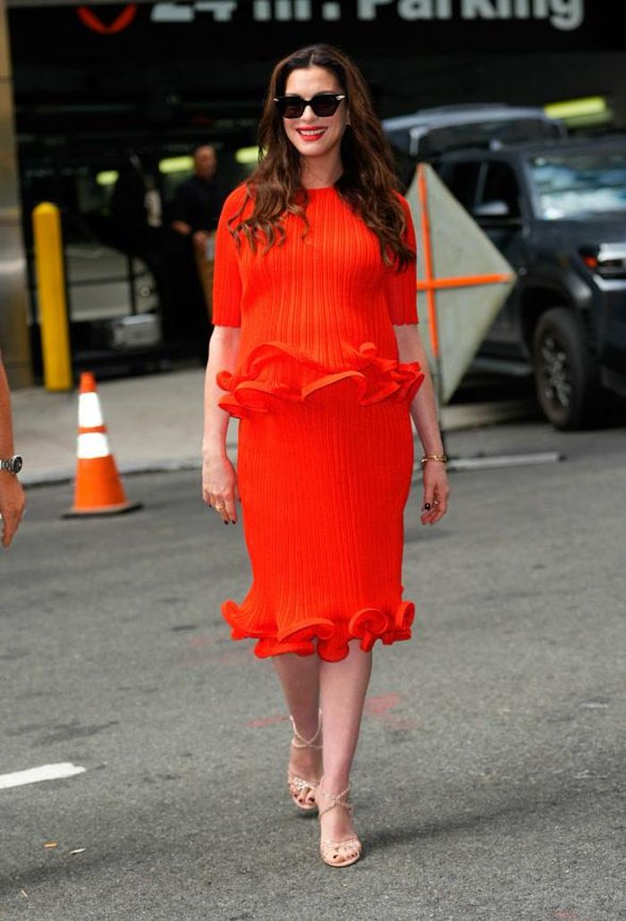 Anne Hathaway hoạt động quảng bá cho Verity trong bộ trang phục dệt kim màu đỏ son thuộc bộ sưu tập ready-to-wear Xuân/Hè 2027 của Carolina Herrera. Áo và chân váy midi đồng điệu được tạo điểm nhấn bằng phần gấu bèo nhún, kết hợp cùng sandal Aquazzura và trang sức Bulgari. Ảnh: Getty Images
