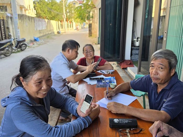 Bà Bùi Thị Thoa (bên trái) mang chiếc điện thoại "cục gạch" thường dùng đến nhờ cán bộ hỗ trợ 