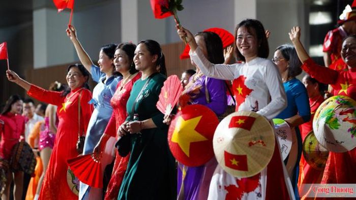 Phụ nữ Thủ đô tươi tắn trong tà áo dài, tay cầm nón lá và cờ đỏ sao vàng lan tỏa tinh thần mến khách. 