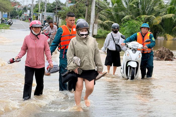 Lực lượng dân quân hỗ trợ người dân đi qua đoạn đường bị ngập và chảy xiết.