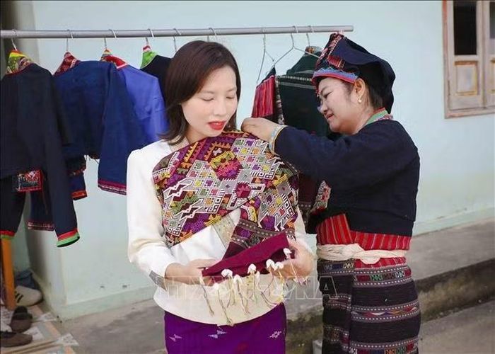 Du khách được phụ nữ dân tộc Lào hướng dẫn mặc trang phục truyền thống và tìm hiểu ý nghĩa của những hoa văn, họa tiết trên trang phục. Ảnh: Xuân Tư/TTXVN