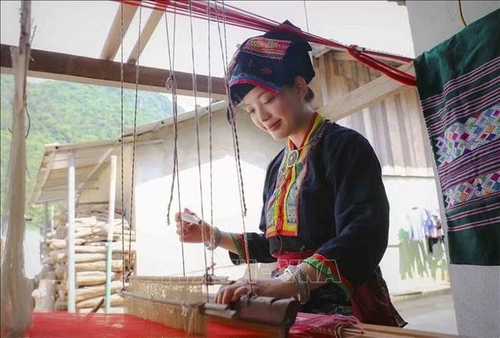 Du khách trong trang phục dân tộc Lào trải nghiệm dệt thổ cẩm bên khung cửi. Ảnh: Xuân Tư/TTXVN
