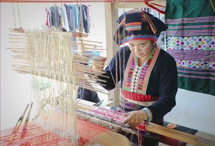 Người phụ nữ Lào điều chỉnh từng sợi chỉ trên khung dệt, tạo nên những đường hoa văn theo các mẫu truyền thống được lưu truyền trong cộng đồng. Ảnh: Xuân Tư/TTXVN