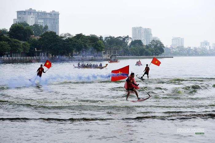 Cờ Tổ quốc tung bay giữa sóng nước và làn khói màu, phía xa là những chiếc thuyền rồng. Ảnh: Tuấn Anh