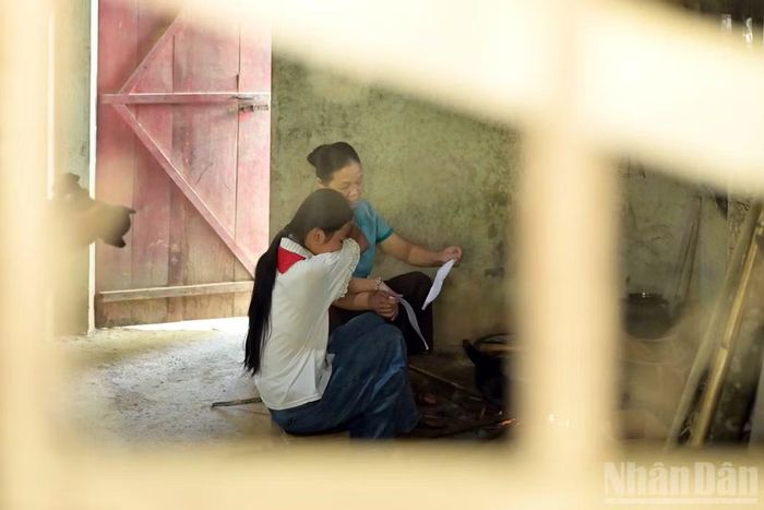 N.T.H. giúp bà nội nấu cơm sau khi đi học về. Thực tế, đây vốn không phải nơi đặt bếp của gia đình, mà chỉ là vị trí được chọn sau khi những cơn lũ dữ quét sạch đồ đạc, tài sản ở tầng một của căn nhà. Lâu dần, góc bếp tạm bợ trở thành nơi nổi lửa nấu biết bao bữa ăn đạm bạc, khiến một góc nhà ám khói đen đặc. (Ảnh: LINH PHAN)
