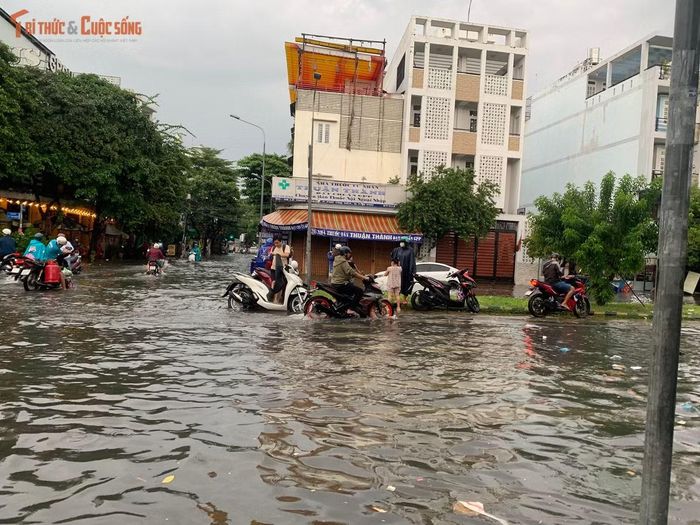 Nước ngập bao vây khắp nơi, người đi xe máy đứng ở dải phân cách chờ nước rút trên đường Lê Thúc Hoạch