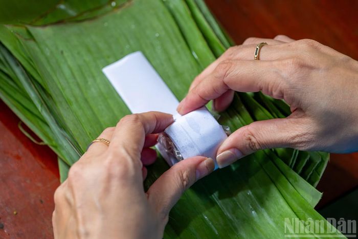 Tiếp theo, dùng 3 đến 4 lớp lá chuối xiêm gói ngang, dọc xen kẽ sao cho thật chắc tay để lá chuối bao kín chiếc nem như vậy khi nem chín sẽ thơm mùi lá.
