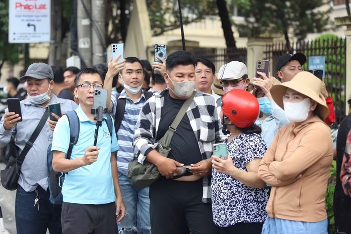 Nhiều người đứng sát hàng rào tòa án, dùng điện thoại ghi lại diễn biến bên ngoài phiên xử.