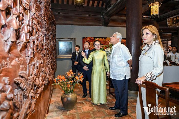 Tổng thống và phu nhân bên bức tranh gỗ "Vinh quy bái tổ". Bức tranh được đặt tại nhà Tiền đường, nhà Thái Học. Đây là tác phẩm độc bản.