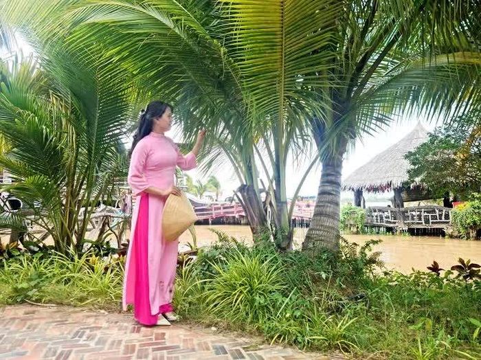 Bà Nguyễn Thị Ngọc Yến - Giám đốc điều hành khu du lịch Cồn Én đứng tạo dáng bên hàng dừa 3 ngọn.