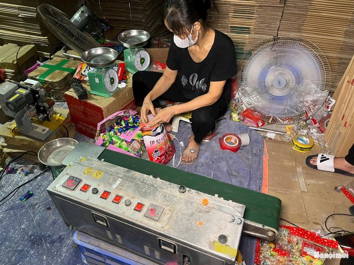 Người lao động tự cắt bao bì, "thay áo" cho sản phẩm bánh kẹo không rõ nguồn gốc. Ảnh: ĐT
